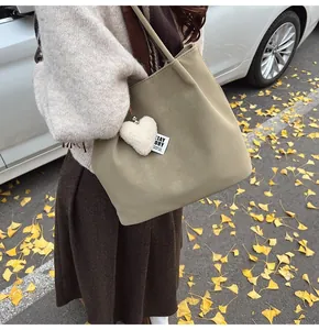 Detail of olive green suede tote bag with plush heart charm in autumn street setting