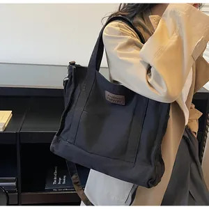 Close-up of a large black canvas tote bag featuring a brown square leather logo patch