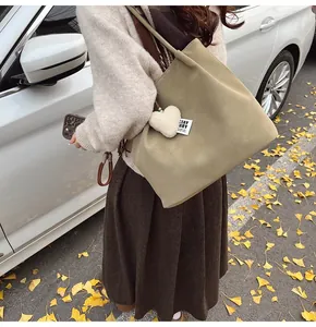 Close-up of olive suede tote bag with heart charm in a sunny autumn outdoor setting