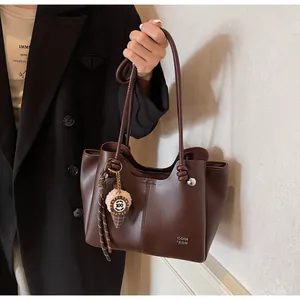 Detail of coffee brown leather tote bag with unique knotted handle and cute charm accessory