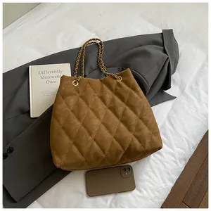Detail van de bruine gewatteerde suède shopper met gouden kettingbanden en textuur