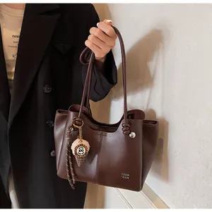 Detail of dark coffee leather tote bag with metallic logo and plush ice cream charm