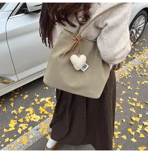 Detail view of suede tote bag with heart charm and plush tag against autumn street