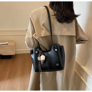 Detail of black leather tote bag featuring a plush charm and fine shoulder strap