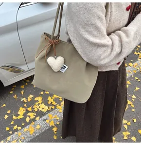 Close-up of suede tote bag detail with plush heart charm and logo tag in autumn setting