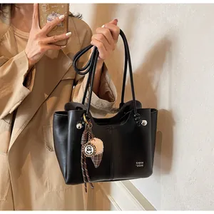 Detail of black leather tote bag with unique charms held by a model in a trench coat