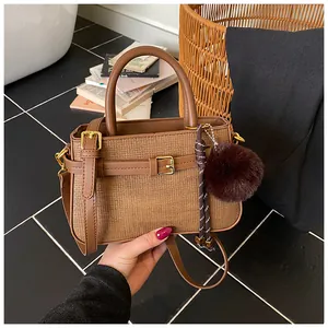 Detail of a brown woven bucket bag featuring leather strap and decorative plush pompom