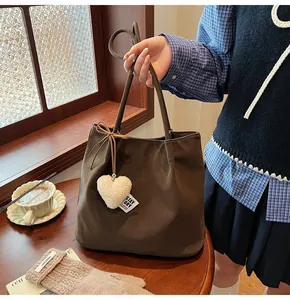 Close-up of dark brown suede tote bag featuring a white plush heart charm and woven label