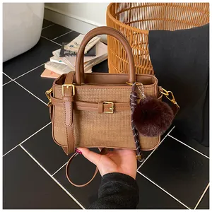 Close-up of brown woven bucket bag featuring leather trim and soft fur ball charm
