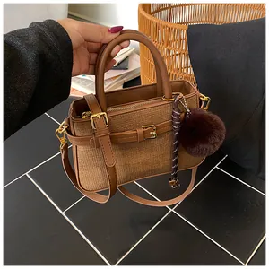 Detailed close-up of brown woven bucket bag featuring faux leather straps and fuzzy charm