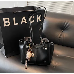 Detail of a black leather tote bag with an ice cream plush charm on a leather sofa