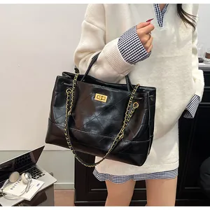 Detail of a black quilted tote bag with gold hardware and chain strap on a female model