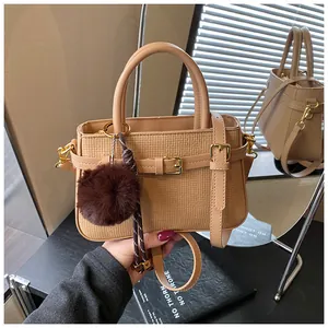 Detail of apricot bucket bag with woven texture, golden buckle, and faux fur pom-pom