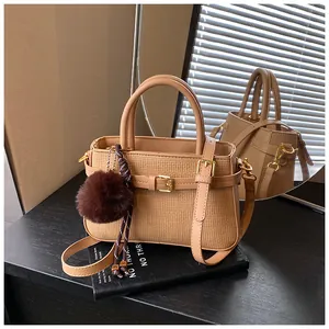 Detail shot of beige bucket bag with woven texture, metal buckle and faux fur charm