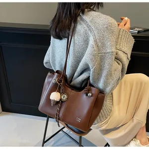 Detail of a large brown leather tote bag featuring plush charms and stylish stitching