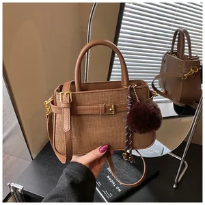 Detailed mirror view of brown woven bucket bag with pompom charm and gold buckle