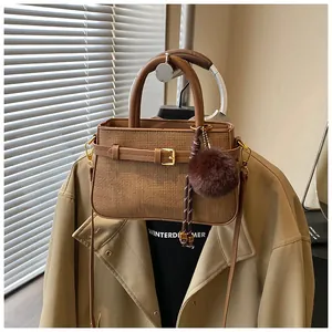 Detail of a brown woven bucket bag with leather strap and large plush ball charm