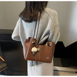 Brown leather tote bag featuring white text logo and a cute ice cream plush charm