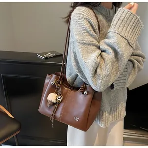 Close-up of brown leather tote bag with metal brand logo and ice cream charm detail