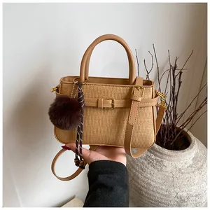 Detailed close-up of straw textured bucket bag with leather trim and pompom charm