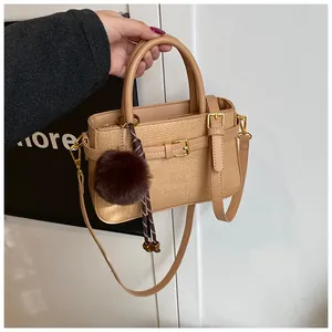 Detail of light brown woven bucket bag featuring gold hardware and a dark plush ball charm