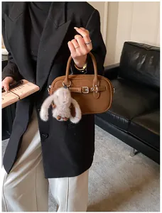 Close-up of brown leather handbag with silver buckle detail and plush rabbit charm