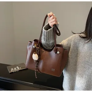 Detail of dark brown leather tote bag with gold hardware and ice cream charm accessory