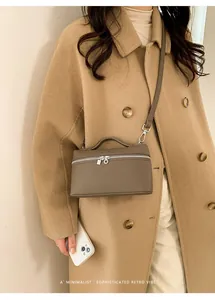 Close-up of minimalist taupe leather crossbody bag with dual zipper and top handle detail