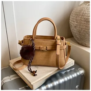 Detail of light brown woven bucket bag with leather handles and faux fur pompom charm