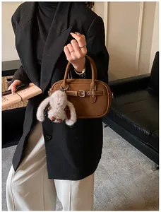 Close-up of brown leather Boston bag with metal buckle detail and plush rabbit pendant