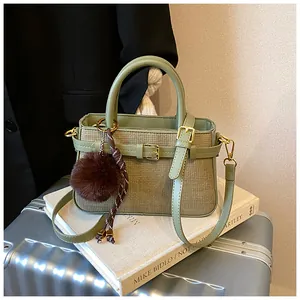 Detail of olive green woven bucket bag with leather strap and brown fur pompom charm
