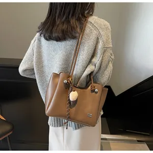 Detail view of large brown leather tote bag with ice cream charm and side lettering