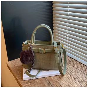 Detail of light green woven texture bucket bag with plush charm and buckle on wooden ledge