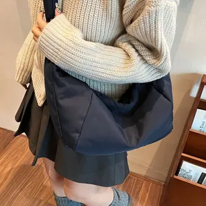 Large minimalist black nylon crescent bag worn by model with beige knit sweater
