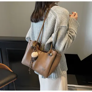 Detailed view of brown leather tote bag with metallic logo and plush keychain charm