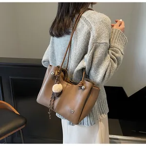 Detail of brown faux leather tote bag with metallic logo and plush ball charm accessory