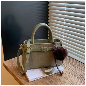 Detail of light green woven bucket bag with brown fur pom-pom and gold M charm