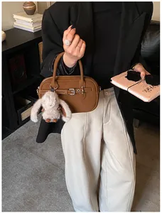 Detail of dark brown pebble leather handbag featuring a plush rabbit charm and metal hardware