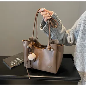 Close-up of brown PU leather tote bag with plush ball charm and metal logo detail