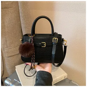 Detail of black textured bucket bag with gold hardware and a brown plush charm accessory
