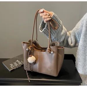 Detail of a brown leather tote bag with contrast stitching and a plush ice cream charm