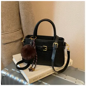 Detail of black woven bucket bag with faux fur charm and gold hardware on luggage