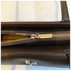 Detail shot of the silver metal zipper and smooth dark brown leather stitching on the tote bag
