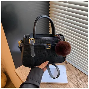 Close-up of black woven texture bucket bag with gold buckle and plush pom-pom charm
