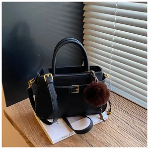 Detail of black textured bucket bag with gold hardware, pompom charm and long strap