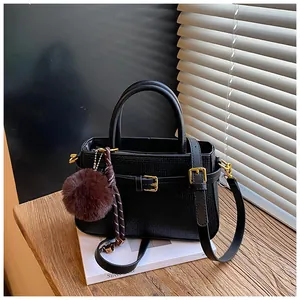 Detail of black textured bucket bag with golden hardware and brown fur ball charm