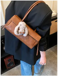 Detail of vintage brown quilted shoulder bag with cute white plush bunny charm on black blazer