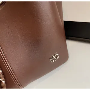 Detail of dark brown leather tote showing silver metal logo and neat stitching craftsmanship
