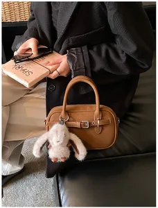 Brown vintage handbag detail with cute plush bunny charm and zip closure held by model