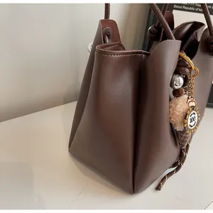 Detail view of large brown leather tote bag with a plush ice cream charm accessory